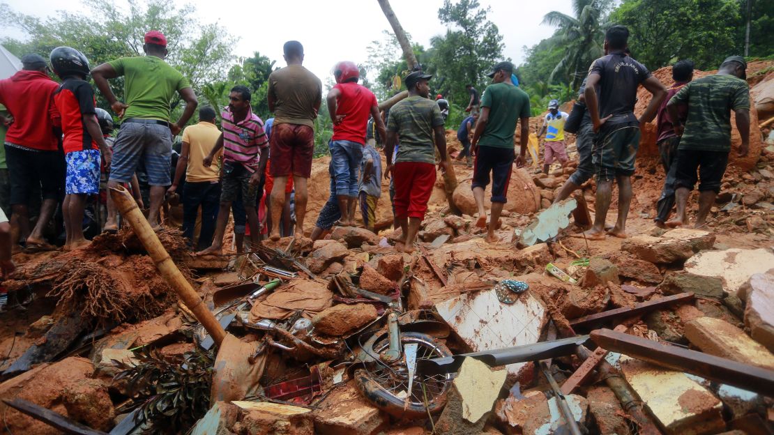 Sri Lankan military rescuers and villagers stand on the debris of a house that was destroyed by a landslide in Bellana village on Friday.