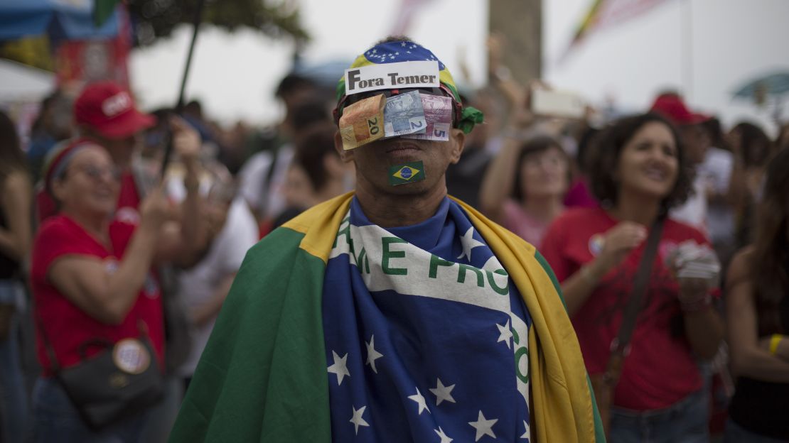 A protester covers his face with money and a sign saying "Temer Out."