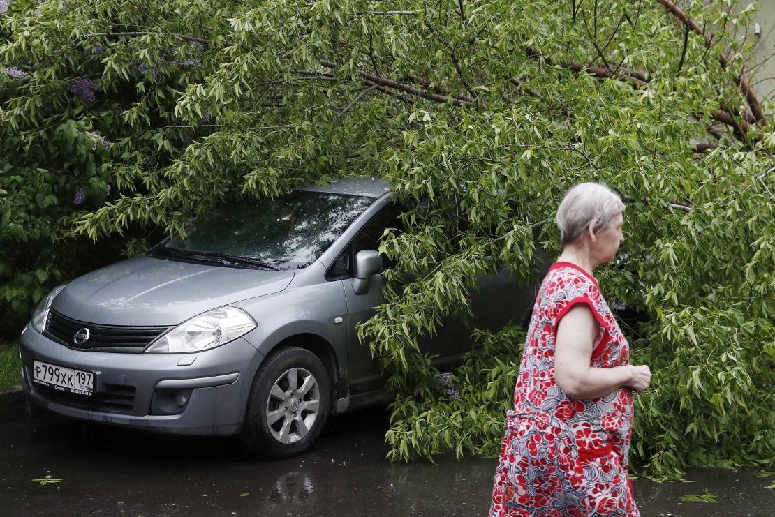 A woman walks past a fallen tree on a car after a heavy storm in Moscow.
