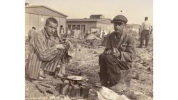 Caption: Two survivors prepare food outside the barracks. The man on the right, presumably, is Jean (Johnny) Voste, born in Belgian Congo, who was the only black prisoner in Dachau. 
Photo Credit: United States Holocaust Memorial Museum, courtesy of Frank Manucci 
Date: May 1945
