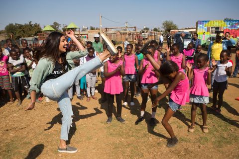 On May 7, 2017 in South Africa, (foreground) UNICEF Goodwill Ambassador Priyanka Chopra, kicking high in the air, laughs as she imitates a dancing young girl, outdoors at the Isibindi Safe Park in Soweto Township, in the city of Johannesburg. 