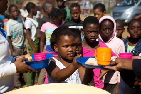 On May 7, 2017 in South Africa, (foreground) a girl receives a snack and a drink at the Isibindi Safe Park in Soweto Township, in the city of Johannesburg. 