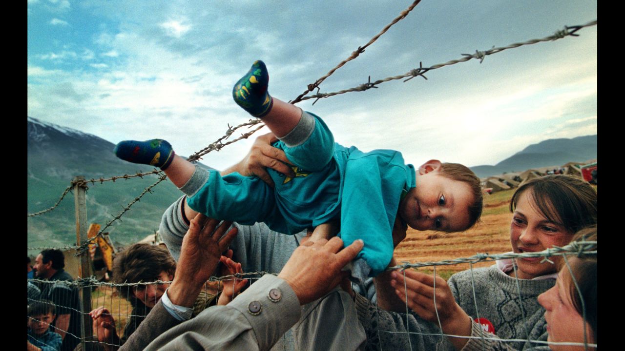 Agim Shala, a 2-year-old Kosovar refugee, is passed through a barbed-wire fence and reunited with his grandparents in a refugee camp in Kukes, Albania, on May 3, 1999. Shala's family was one of thousands driven from their homes in Kosovo by the deadly fighting in the Balkans.