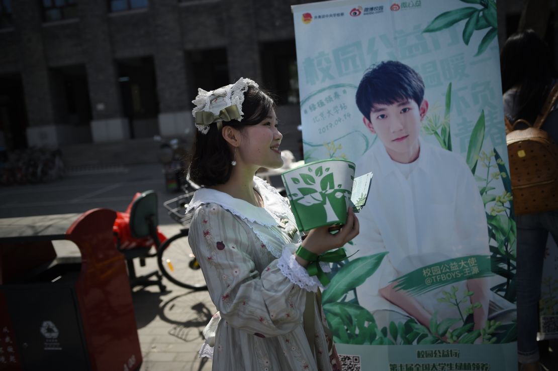 A woman hands out leaflets during an event for fans of TFBoys in April 2017. Another band member Wang Yuan is on the background poster. 