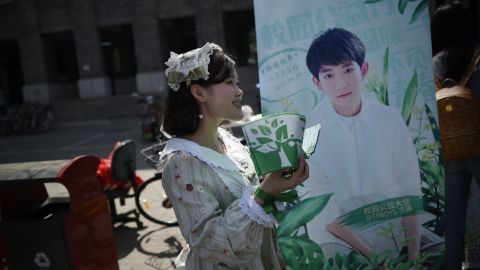A woman hands out leaflets during an event for fans of TFBoys in April 2017. Another band member Wang Yuan is on the background poster.