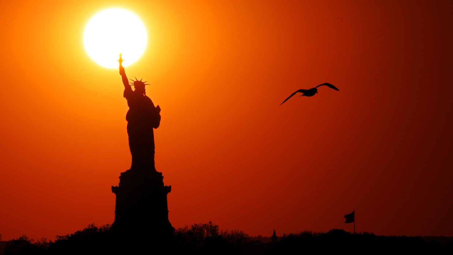 The sun sets behind the Statue of  Liberty as a seagull flies past on June 02, 2017 in New York City.