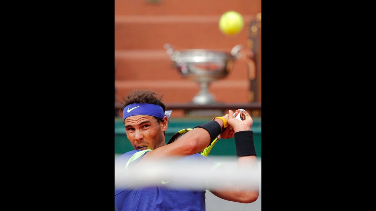 The winner's trophy is seen in the background as Nadal hits a backhand.