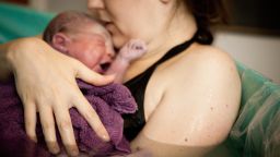 Color photo of a loving mother holding her newborn baby son in the water of a birthing tub immediately after a water birth at home.