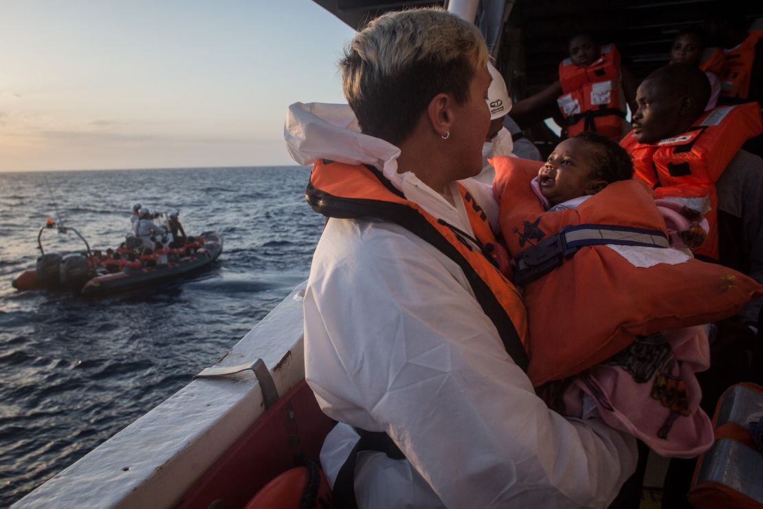A crewmember from the Migrant Offshore Aid Station Phoenix vessel holds a child as they wait to transfer refugees