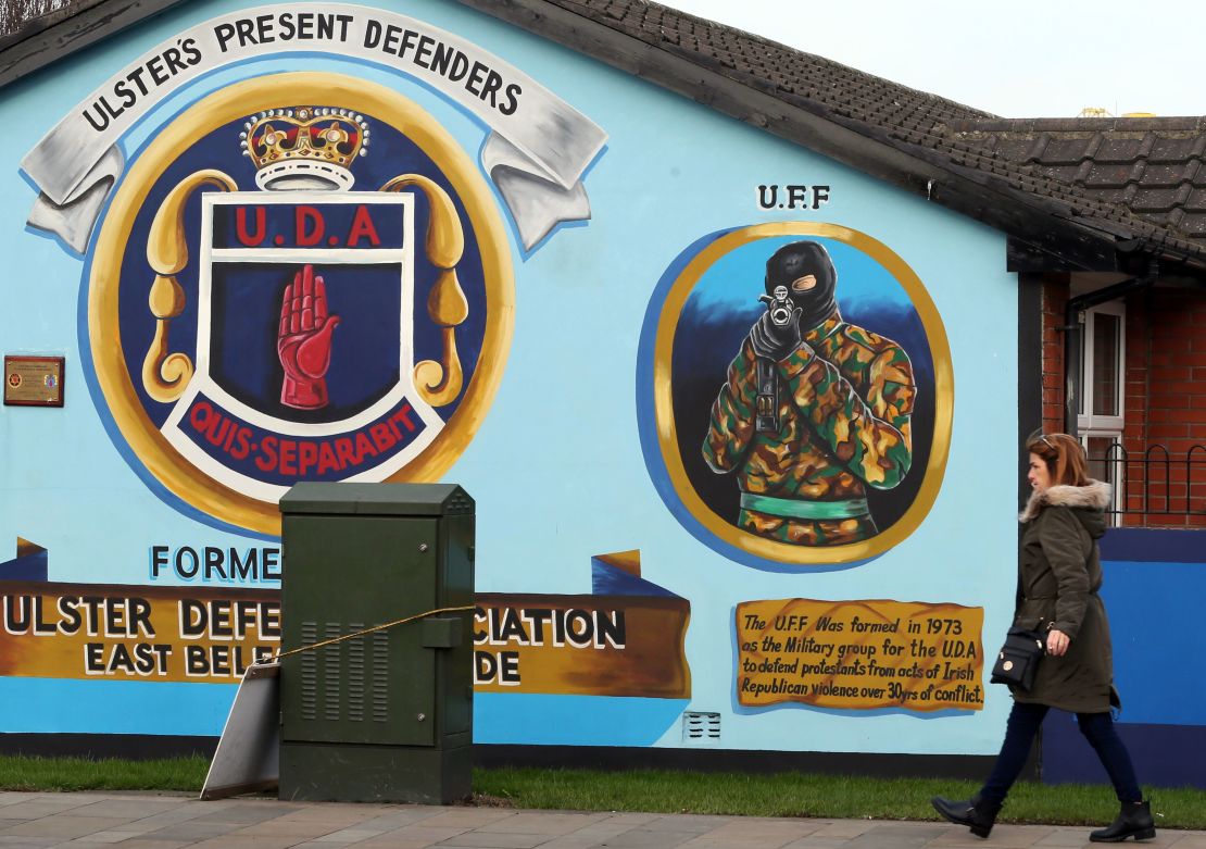 A woman walks past a loyalist mural, depicting an Ulster Freedom Fighter (UFF) in Belfast. 