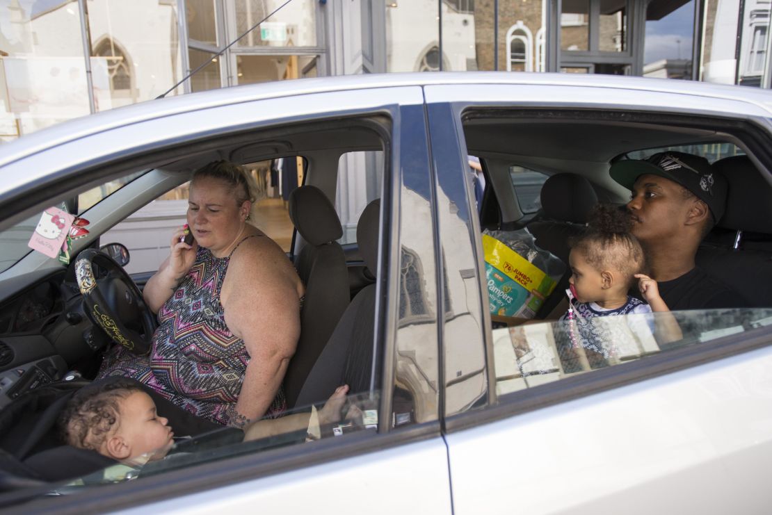 Emma Spinola talks on the phone outside Notting Hill Community Church as her baby sleeps in the front seat and husband Liniker minds their other child in the back.