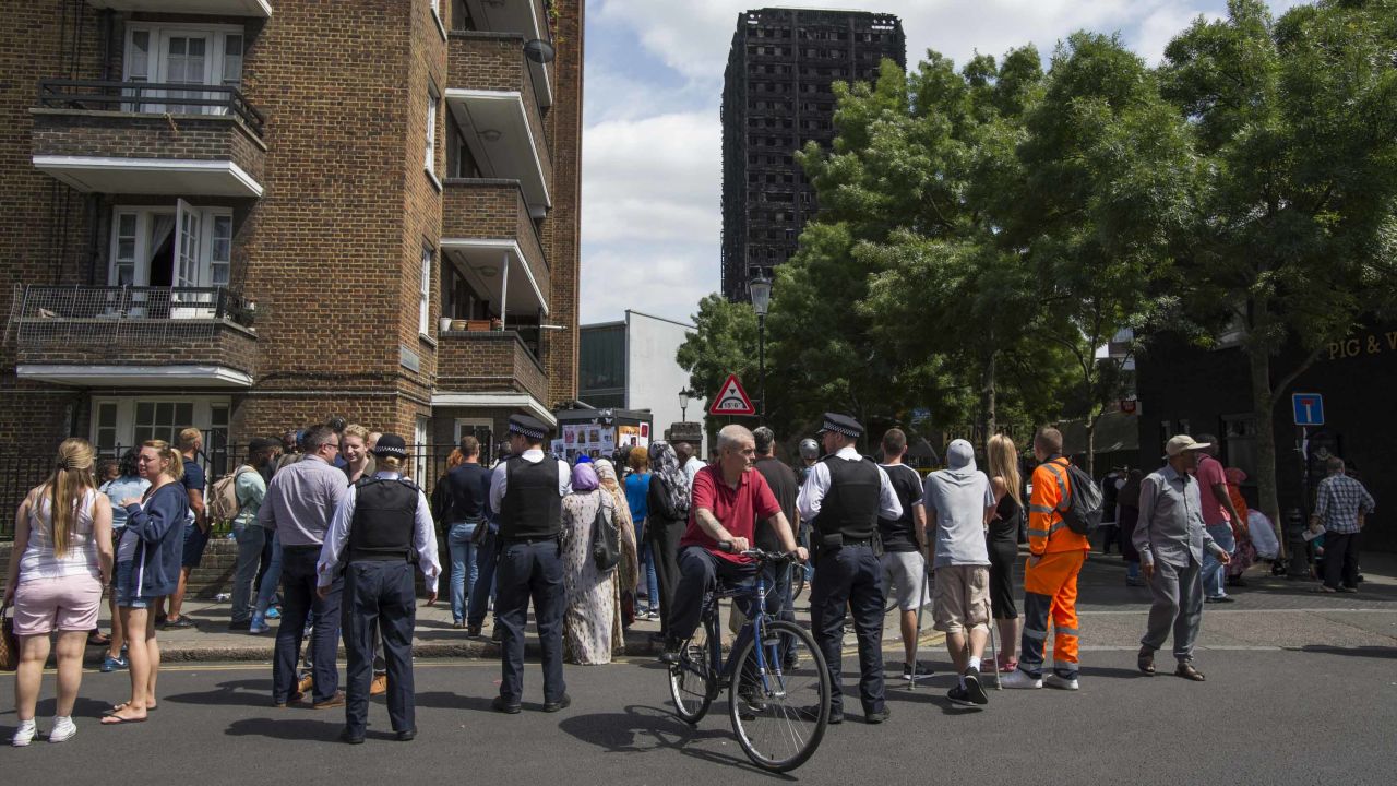 A crowd gathers in view of the blackened Grenfell Tower.