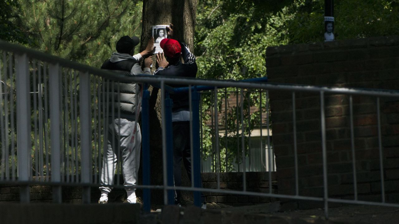 Two people work to tape a missing person's poster to a tree near Grenfell Tower.