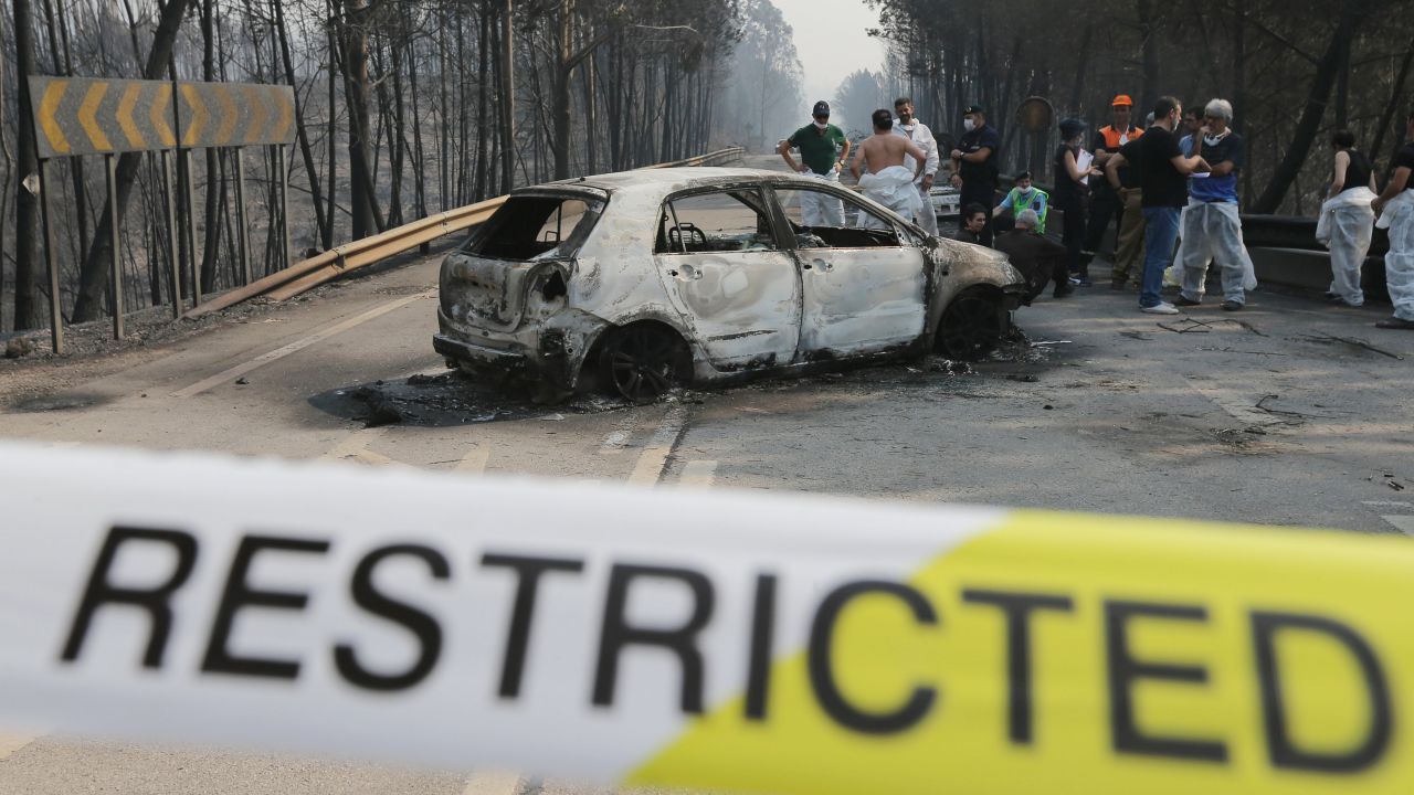 Firefighters and medical forensic investigators stand near a burnt car on the N236 road in central Portugal.