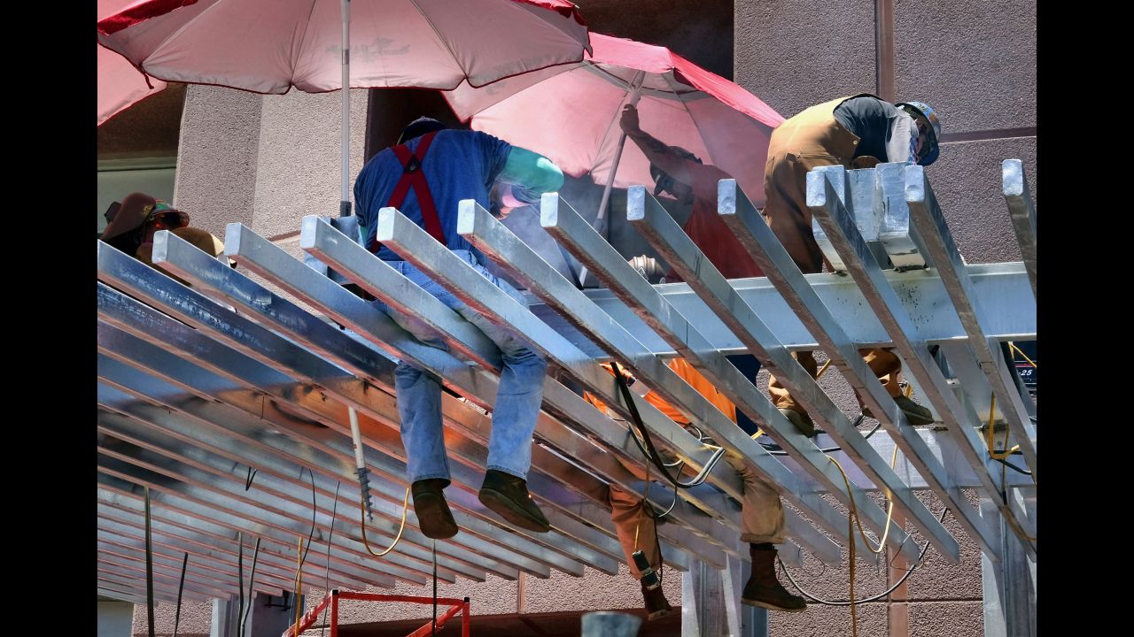 Construction workers try to shade themselves from the direct sun while welding a steel awning in Los Angeles on June 19.