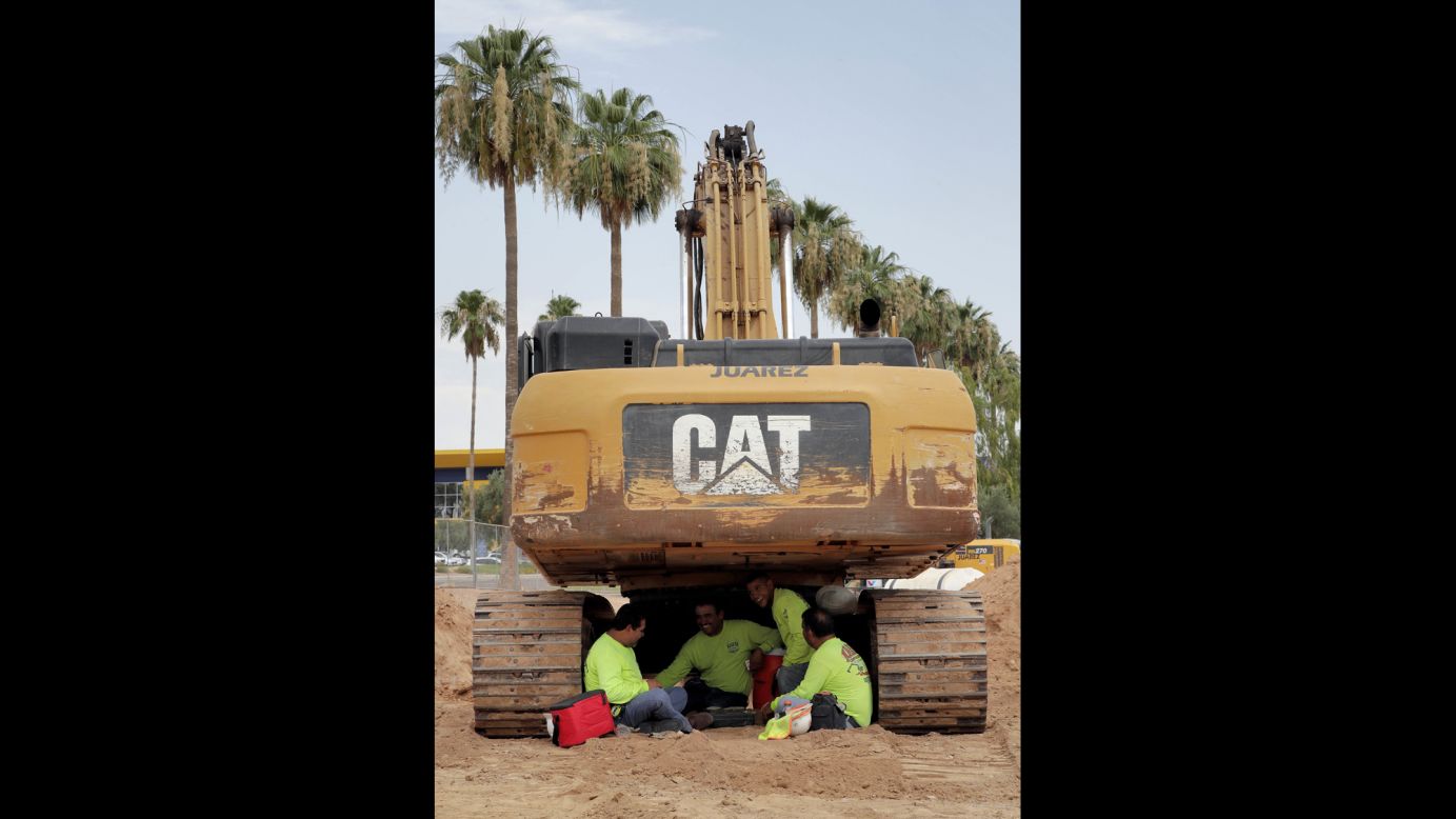 A construction crew sits under their excavator during a break in Tempe on June 20.