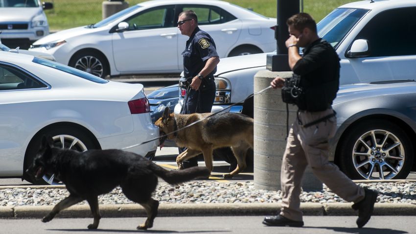 Police dogs search cars in a parking lot at Bishop International Airport, Wednesday morning, June 21, 2017, in Flint, Mich. Officials evacuated the airport Wednesday, where a witness said he saw an officer bleeding from his neck and a knife nearby on the ground. Authorities say the injured officer's condition is improving. (Jake May/The Flint Journal-MLive.com via AP)