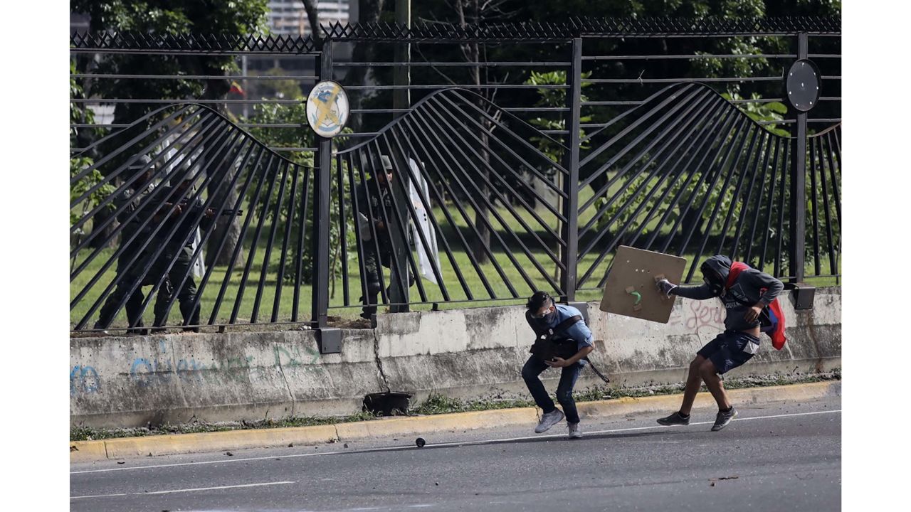 A protester carrying a Venezuelan flag moves in to provide cover after Vallenilla was shot.