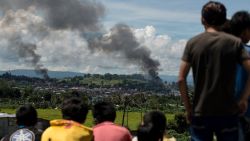 TOPSHOT - People watch as smoke billows from houses after aerial bombings by Philippine Airforce planes on Islamist militant positions in Marawi on the southern island of Mindanao on June 17, 2017. 
Philippine troops pounded Islamist militants holding parts of southern Marawi city with air strikes and artillery on June 17 as more soldiers were deployed and the death toll rose to more than 300 after nearly a month of fighting. / AFP PHOTO / Noel CELIS        (Photo credit should read NOEL CELIS/AFP/Getty Images)