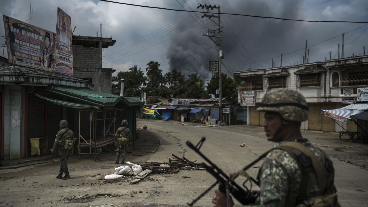 Soldiers patrol a street as smoke billows from a fire caused by heavy gunfights and aerial strikes on June 6, 2017 in Marawi.