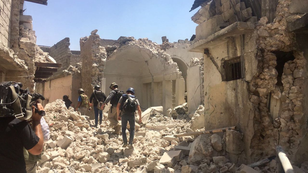 Journalists trudge through rubble escorted by Iraqi troops.