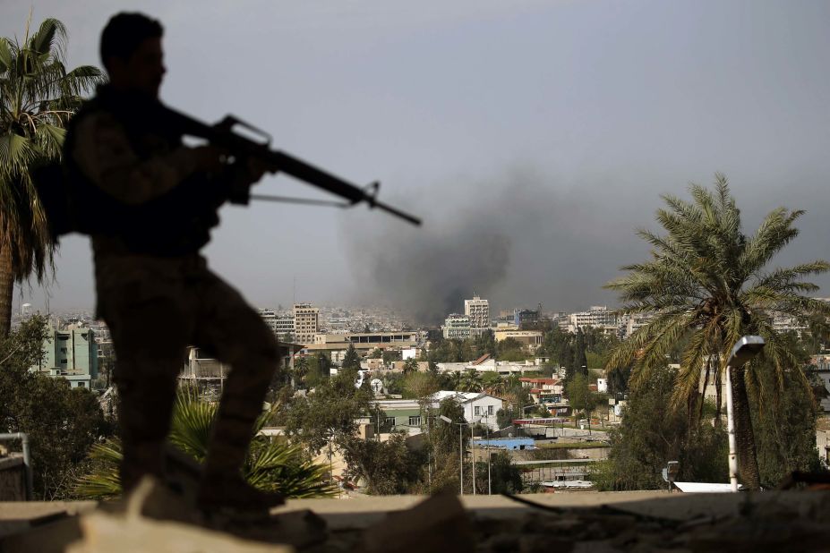 A member of Iraq's security forces stands guard in eastern Mosul as smoke rises from the ISIS-controlled western section of the city on Friday, April 7.