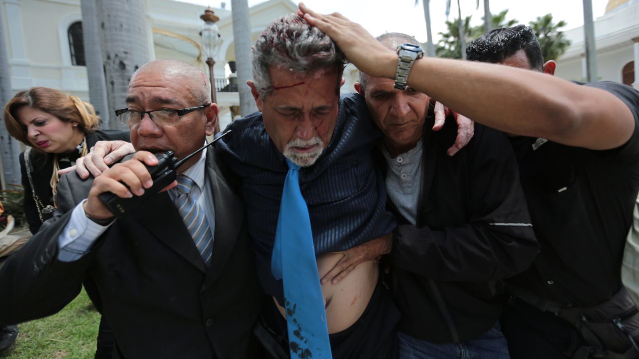 Opposition lawmaker Americo De Grazia is led away by bodyguards and a National Assembly employee after he was injured by government supporters.