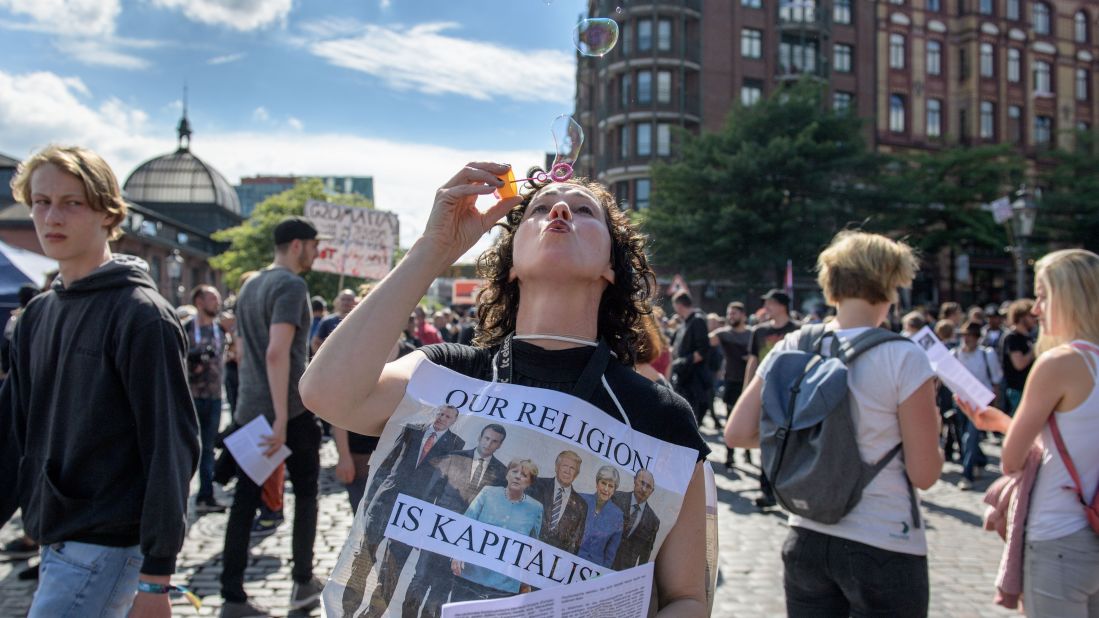 A woman wearing a sign depicting the G20 summit world leaders blows bubbles at Hamburg harbor before the protest march.