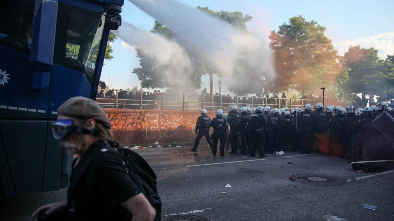 A man wearing protective goggles moves away from officers trying to clear the streets using water cannons.