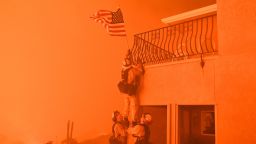 Firefighters remove a US flag as flames from the "Wall Fire" close in on a luxury home in Oroville, California on July 8, 2017. The first major wildfires after the end of California's five-year drought raged across the state on July 8, as it was gripped by a record-breaking heatwave.