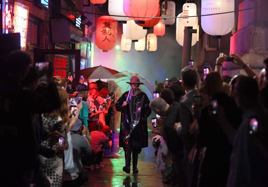 People walk past Louis Vuitton store in rain at night in Tokyo