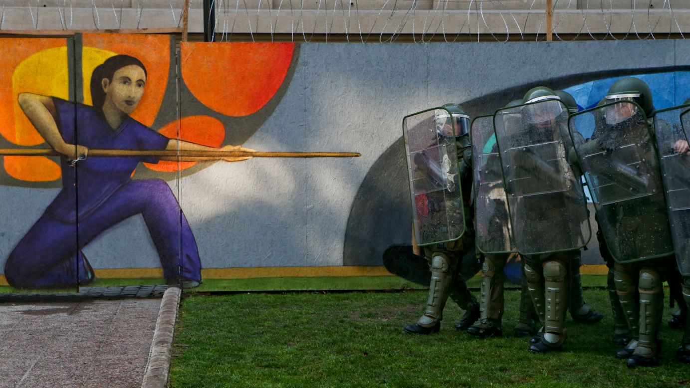 Police officers in riot gear walk next to an art museum as they confront protesters in Santiago, Chile, on Monday, July 10. Gay rights activists were clashing with people who were demonstrating against a gender identity bill in Chile's Congress.