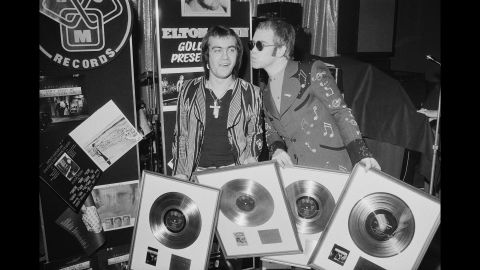 John and his songwriting collaborator, Bernie Taupin, hold gold records in 1973. Taupin has written the lyrics for many of John's songs over his career, and the two have worked together for decades.