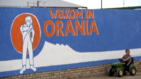 A young South African Afrikaner boy plays by a painted wall reading "Welcome in Orania" in Afrikaans.