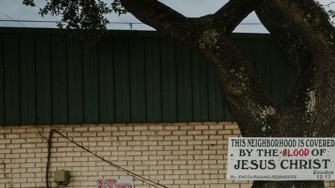 A sign welcoming people into the Goose reads, "This neighborhood is covered by the blood of Jesus Christ." In the background is the Discount Zone gas station where several shootings have occurred in recent years. 