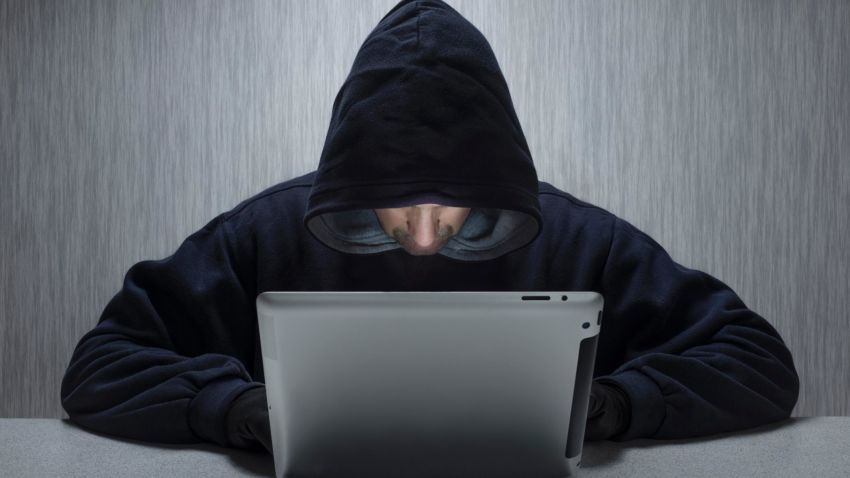 An anonymous hooded male using a tablet computer to represent a cyber criminal. (Photo by: Loop Images/UIG via Getty Images)