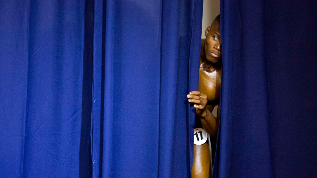 A bodybuilder peeks out from a curtain as competitors perform at the Haiti Bodybuilding Classic on Sunday, July 23.