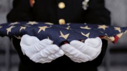Military personnel holding a folded US flag.