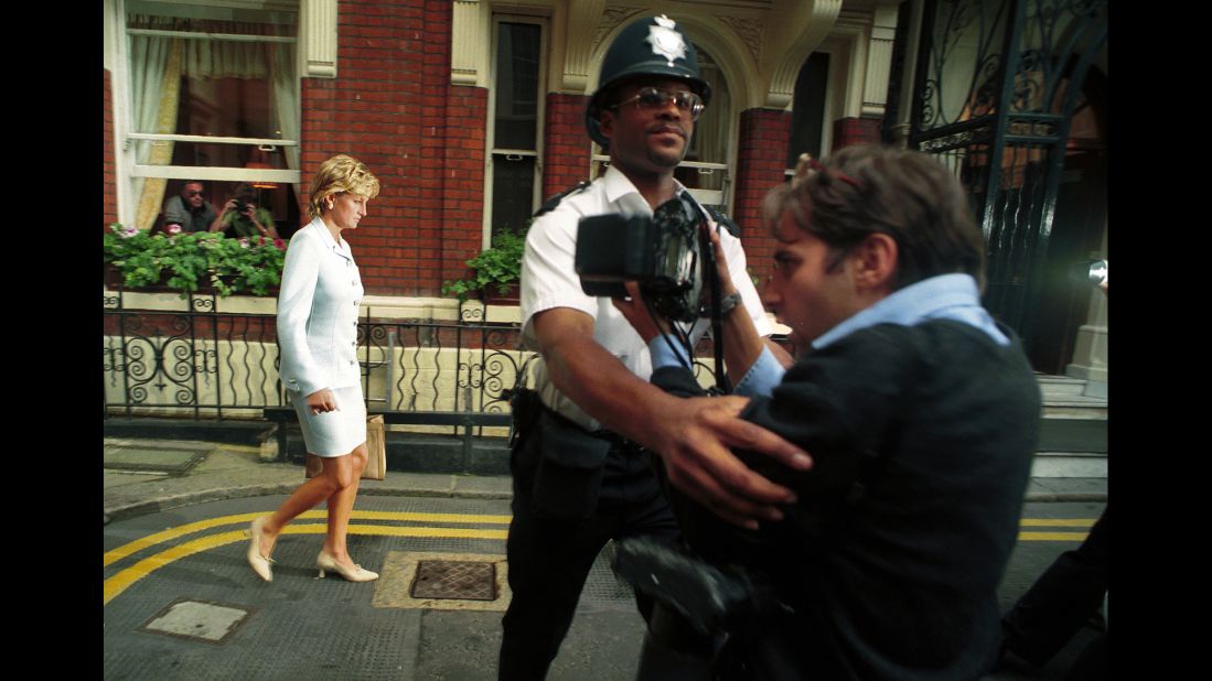 A police officer holds back a photographer as Diana walks by in July 1996. It had just been announced that Diana and Charles had divorced.