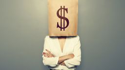 businesswoman hiding under paper bag with dollar sign over dark background; Shutterstock ID 193696625