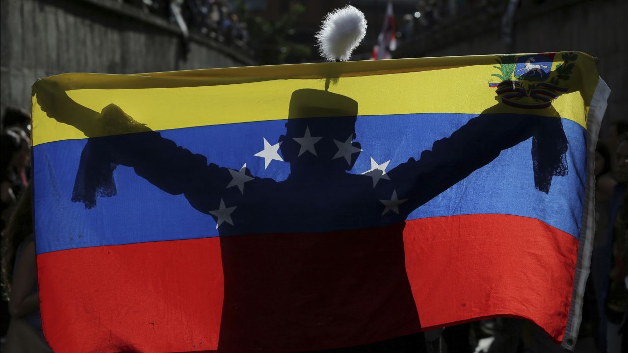 A demonstrator dressed as Venezuelan independence hero Simon Bolivar is silhouetted against a national flag in Caracas on Monday, July 24.