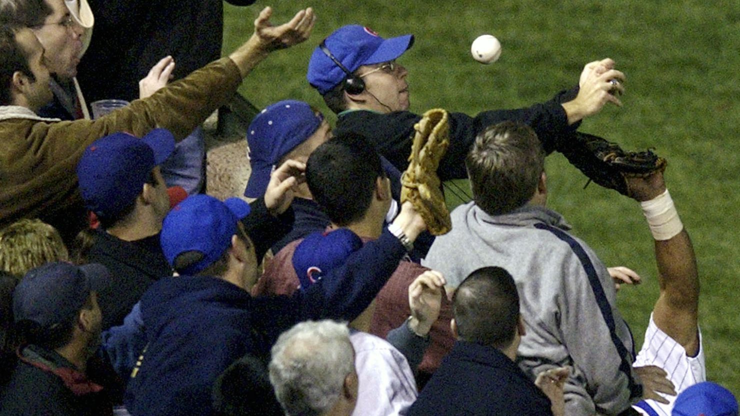 On October 14, 2003, Cubs left fielder Moises Alou's arm reaches into the stands unsuccessfully for a foul ball tipped by fan Steve Bartman, wearing headphones and glasses.