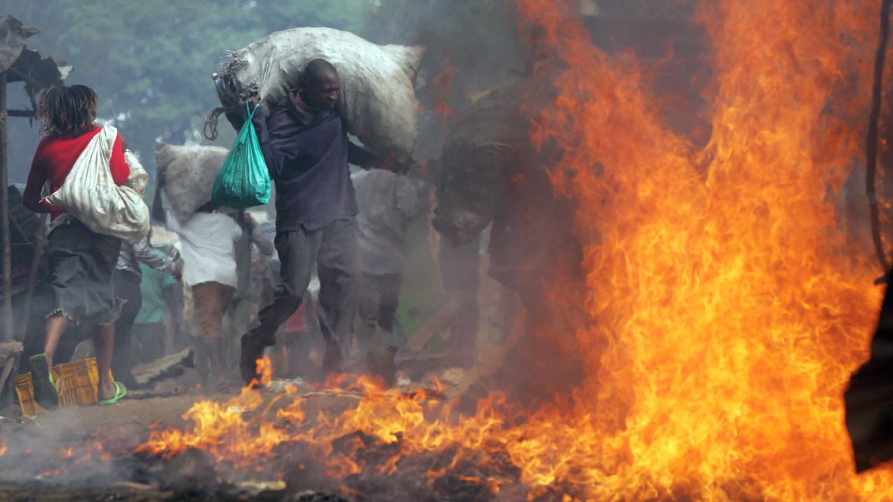 A resident of Kibera runs with a sack of charcoal he stole past a burning shack as he and thousands of other looters swept through the slum ransacking stores and setting cars and other property on fire 31 December 2007.
