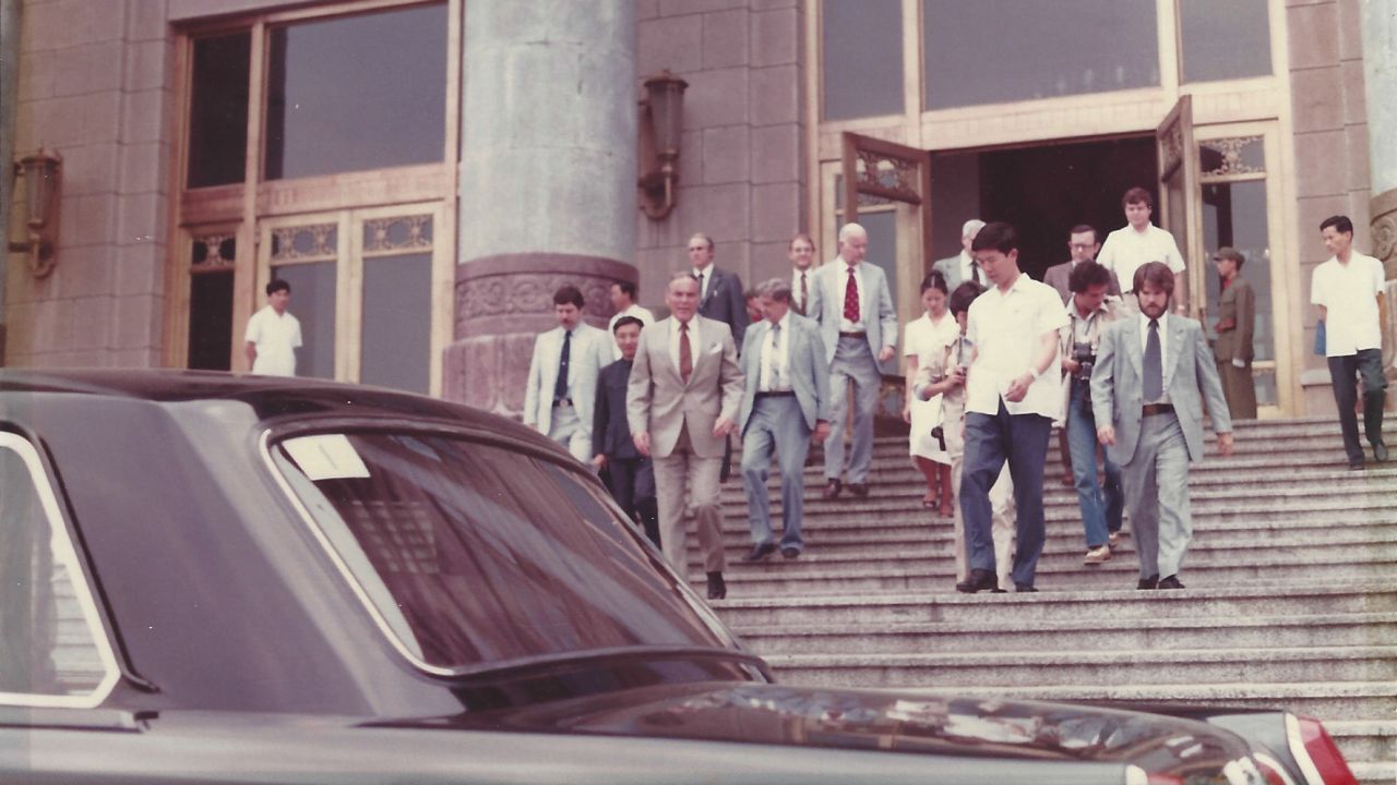 On the right, wearing a suit and tie, Booth helps escort US Secretary of State Alexander Haig, in the foreground on the left, to a waiting security motorcade positioned at the bottom of the staircase at the Great Hall of the People in Beijing, China.