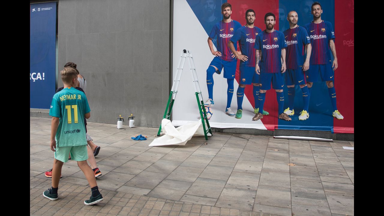 A boy wearing Neymar's jersey walks past a new Barcelona poster -- without Neymar -- as it is put up outside the Camp Nou stadium on Wednesday, August 2.