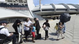 Asylum seekers take a walk outside Olympic Stadium as security guards look on in Montreal, Wednesday, Aug. 2, 2017. The stadium will be housing asylum seekers after a spike in the number of people crossing at the United States border in recent months. (Ryan Remiorz/The Canadian Press via AP)
