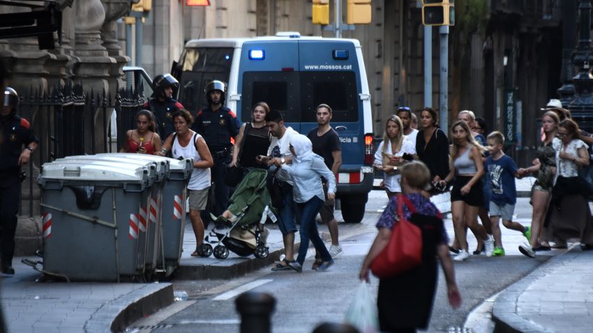 People flee the scene in Barcelona, Spain, Thursday, Aug. 17, 2017, as police officers patrols after a white van jumped the sidewalk in the historic Las Ramblas district, crashing into a summer crowd of residents and tourists and injuring several people, police said. (AP Photo/Giannis Papanikos)