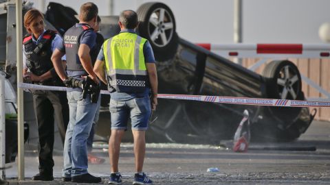 Police officers stand near an overturned car onto a platform at the spot where terrorists were intercepted by police in Cambrils, Friday, Aug. 18.