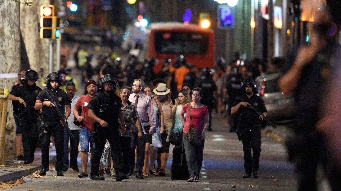 Police accompany clients of a store outside a cordoned off-area of Barcelona. Las Ramblas is especially crowded in the summer, the height of tourist season. The promenade passes by kiosks, flower sellers, cafes and bars.