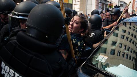 A woman is detained Saturday as officers escort police wagons away from Boston Common.